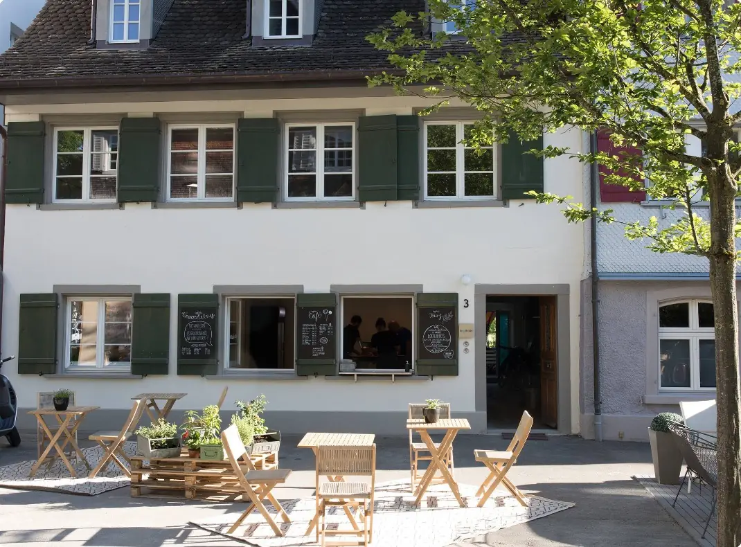 Das Begegnungshaus mit Café-Fenstern und Tischen vor dem Haus