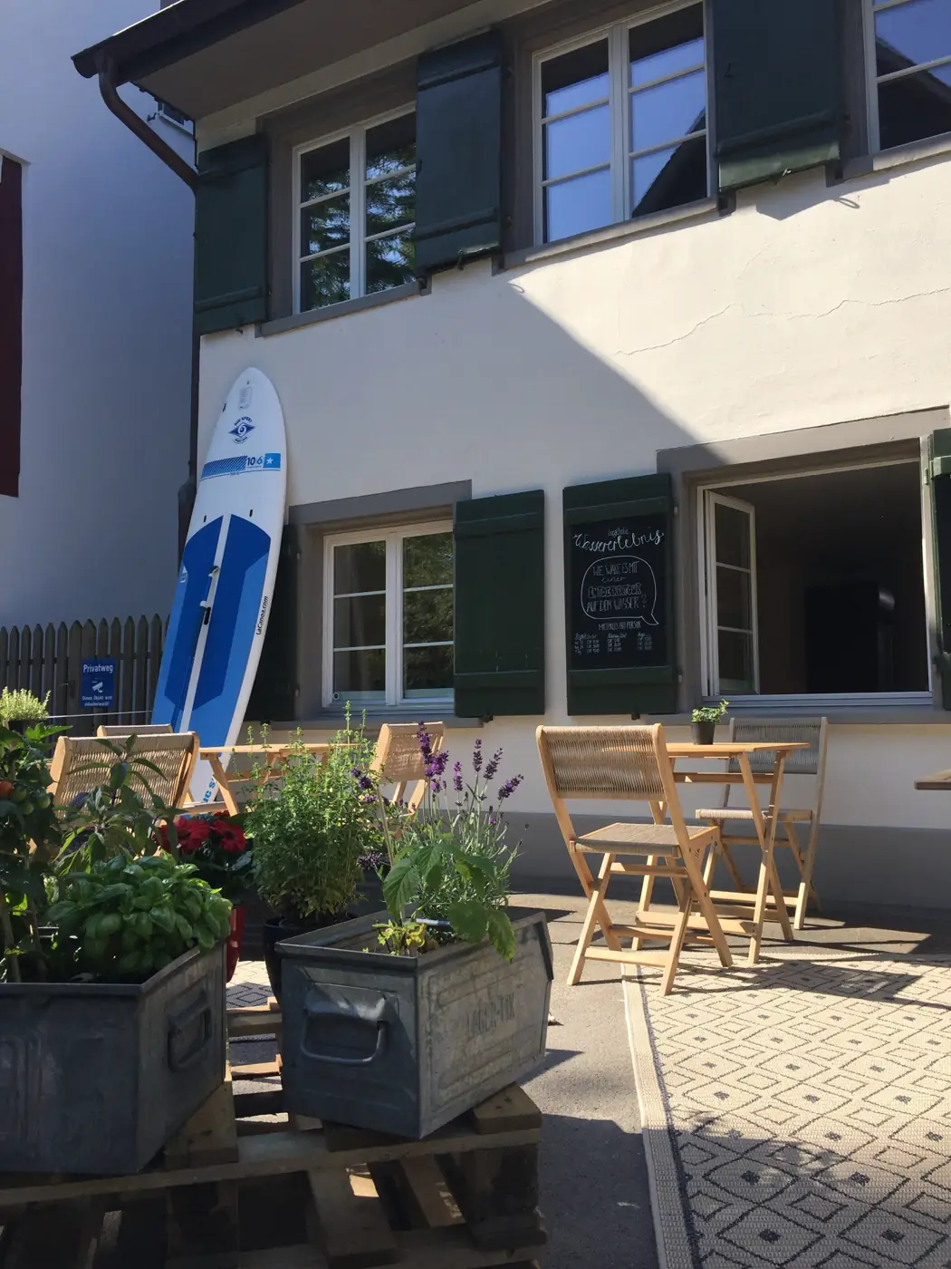 Die kleine Terrasse mit Kräutern, Tischen und Paddleboard